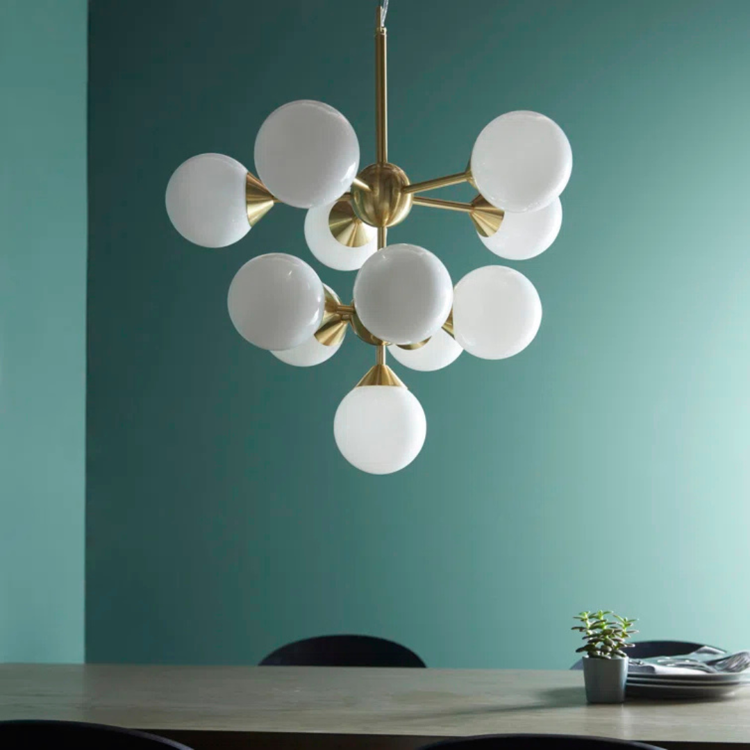 Modern chandelier with white glass shades and gold metal accents against a teal wall.