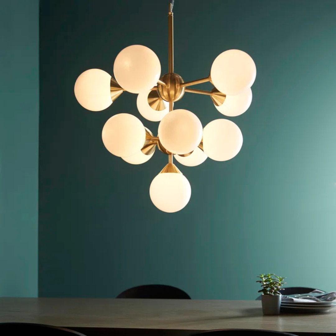 Modern chandelier with gold frame and white glass globes against a teal wall.