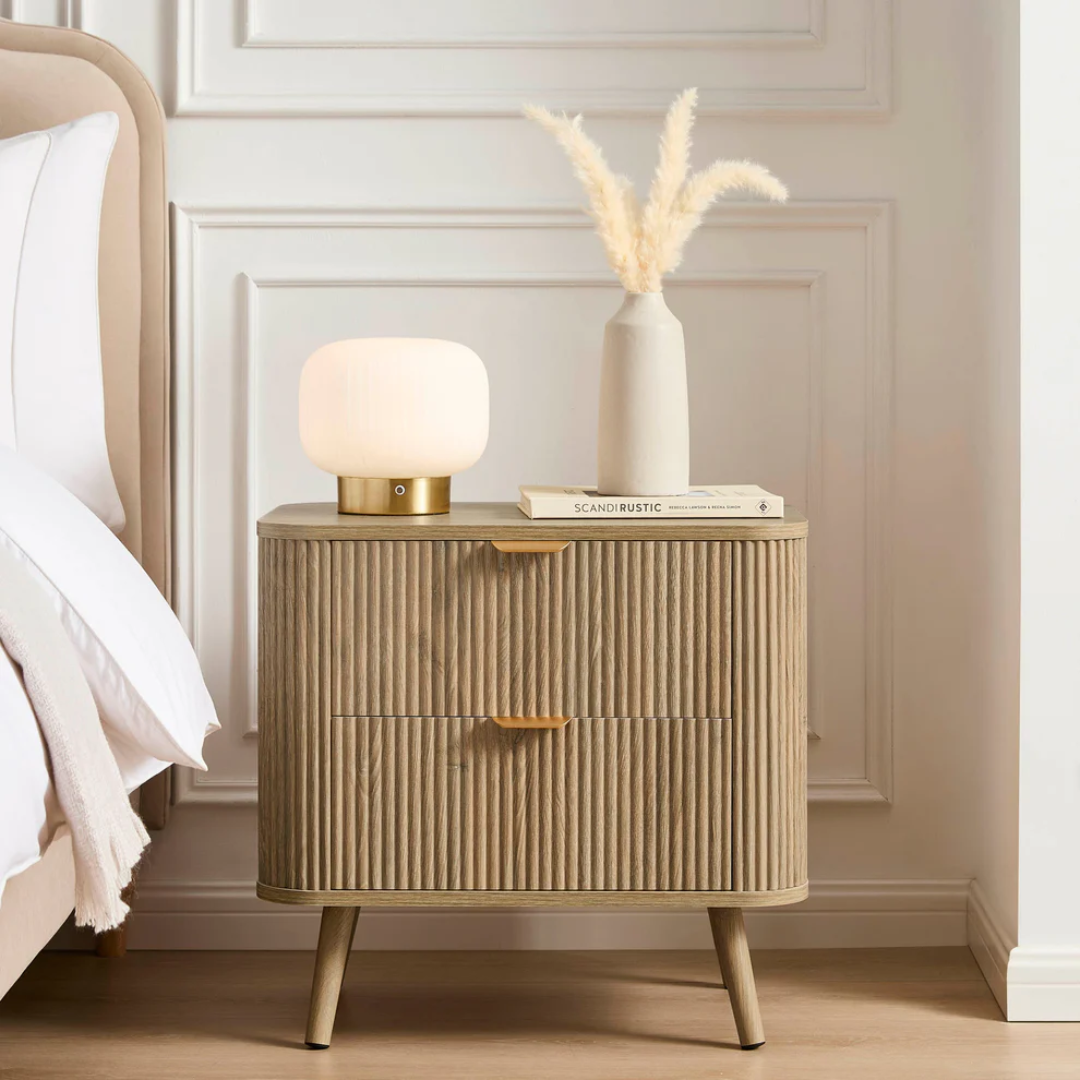 Beige nightstand with lamp and books against a white wall