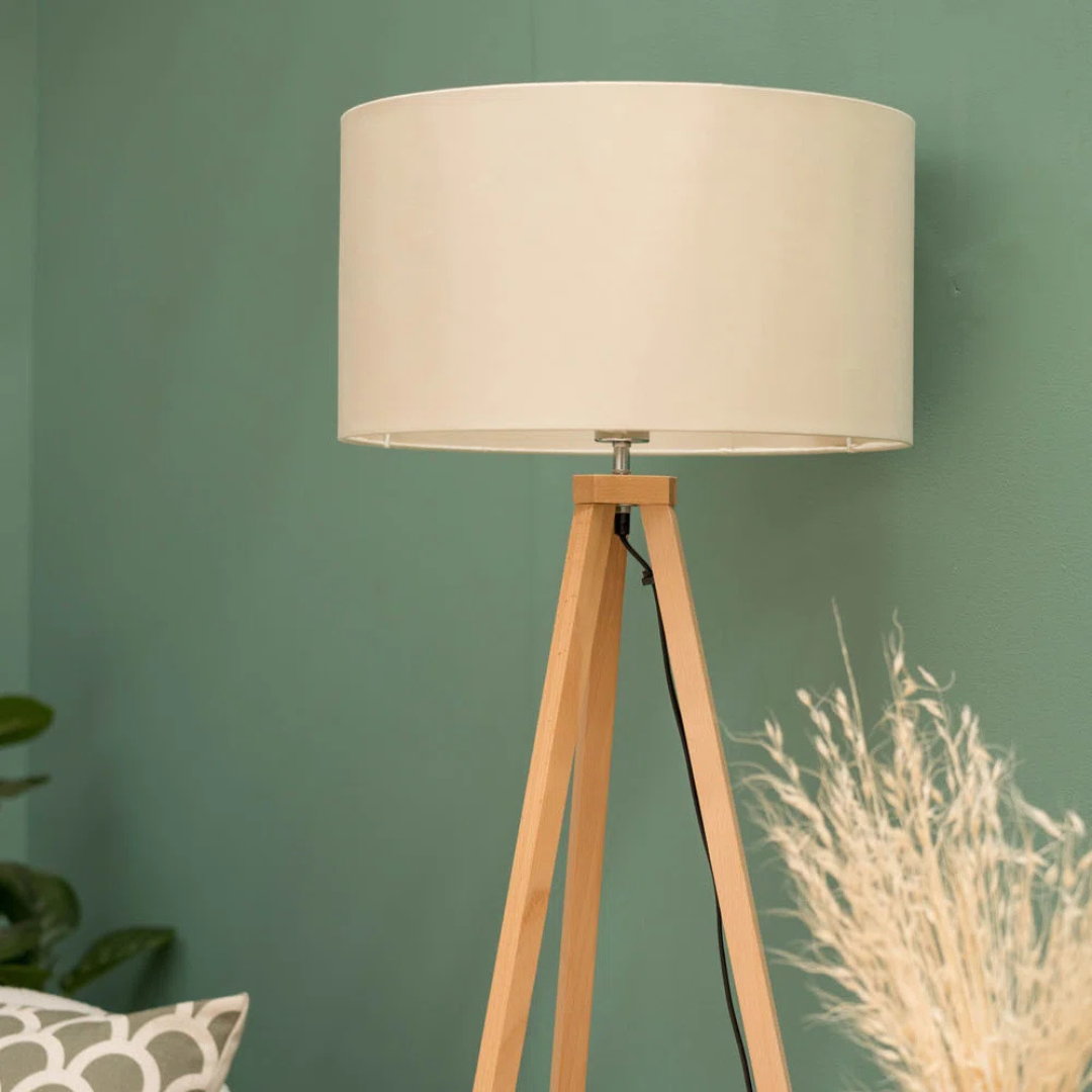 Floor lamp with beige shade and wooden base against a green wall