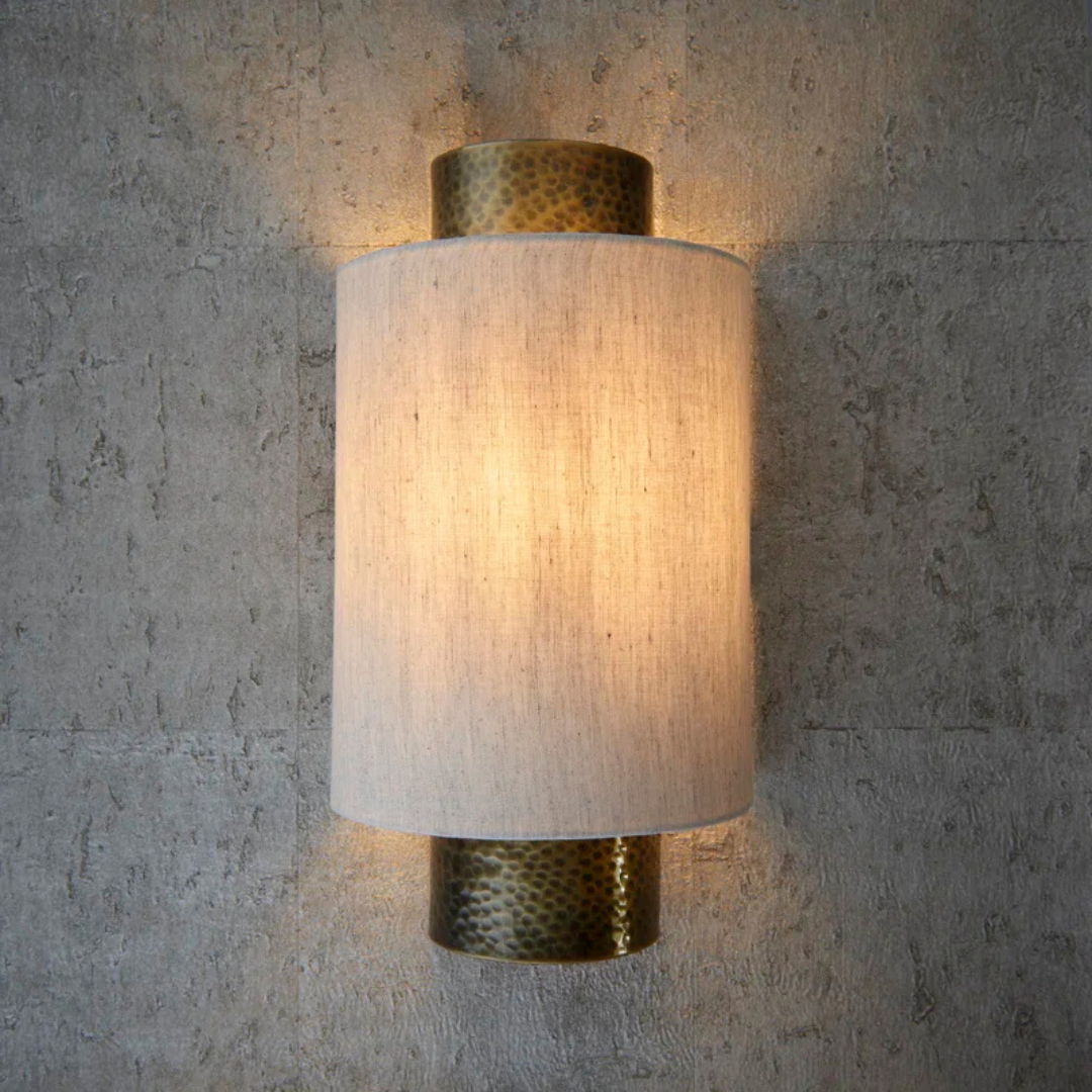 Wall-mounted light fixture with textured shade and metallic accents on a concrete wall.