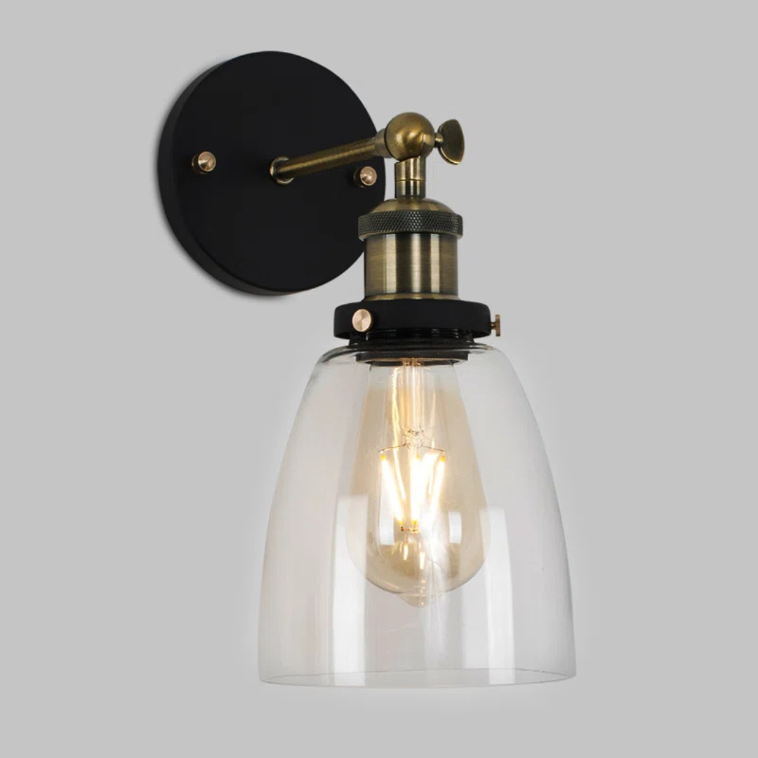 Wall-mounted light fixture with clear glass shade and brass accents on a gray background