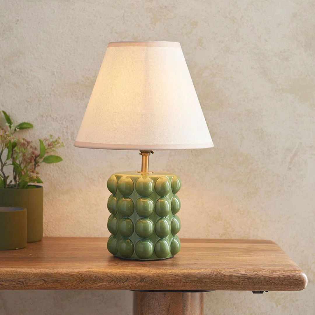 Green textured table lamp with a white shade on a wooden surface.