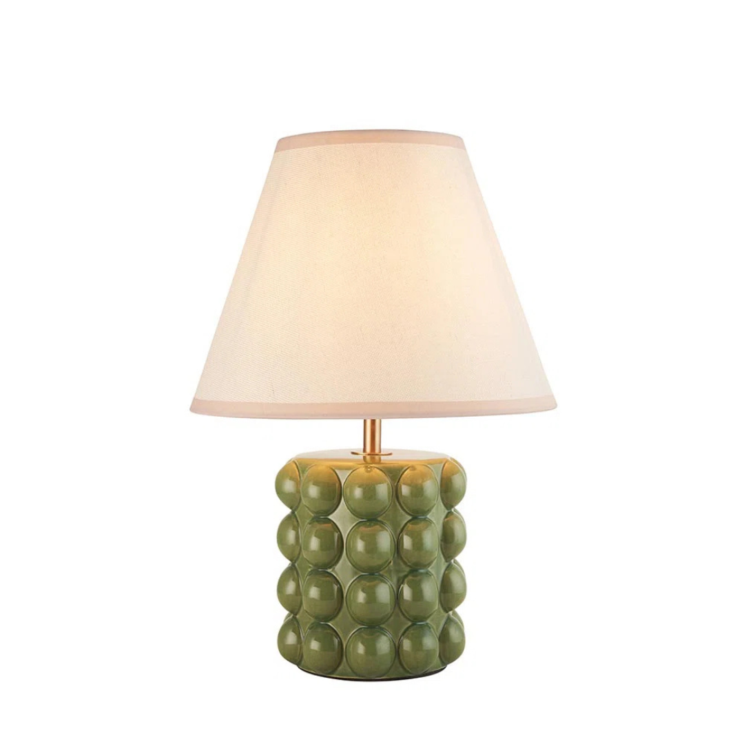 Table lamp with green textured base and beige shade on a white background