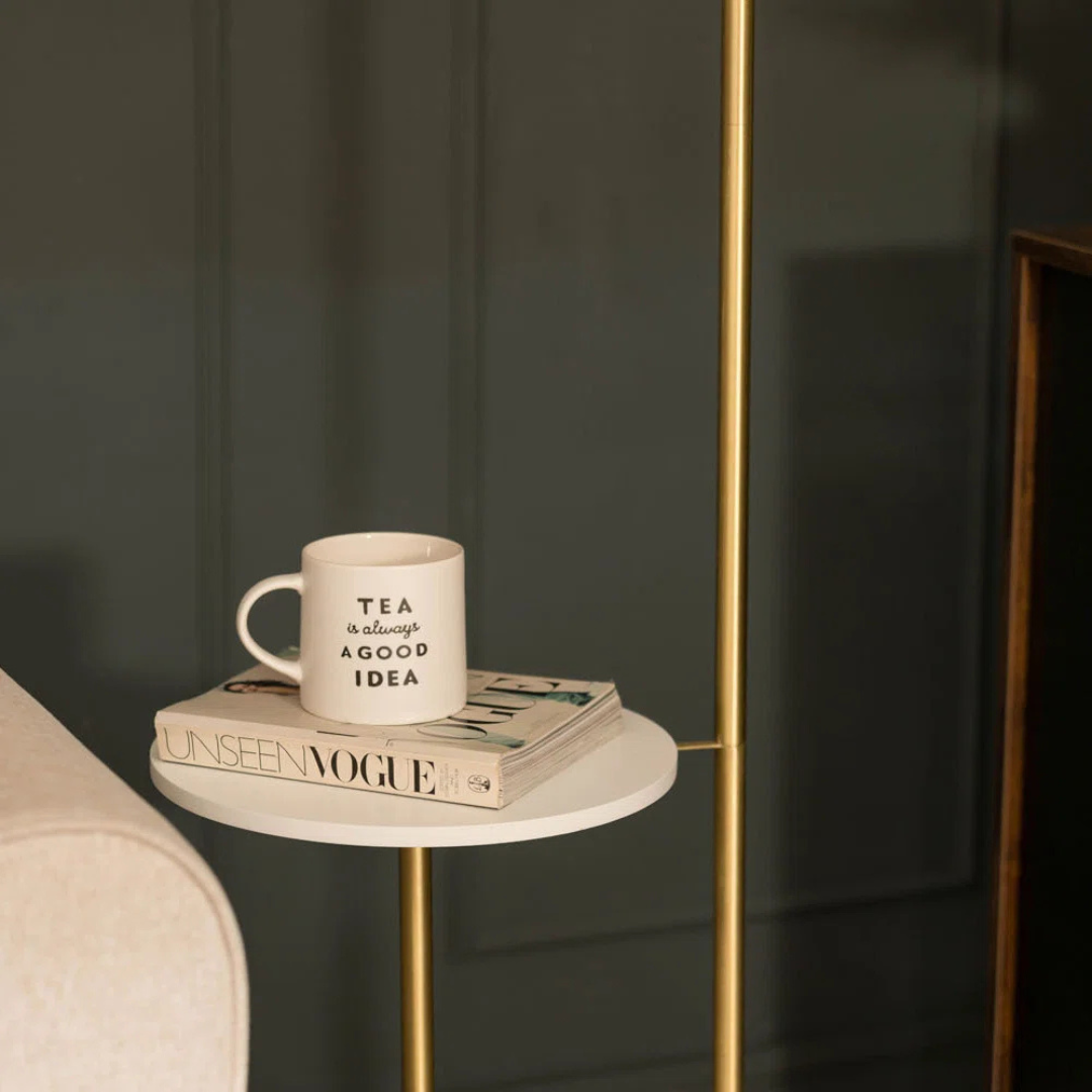 White mug with text on a book on a small round table next to a sofa.