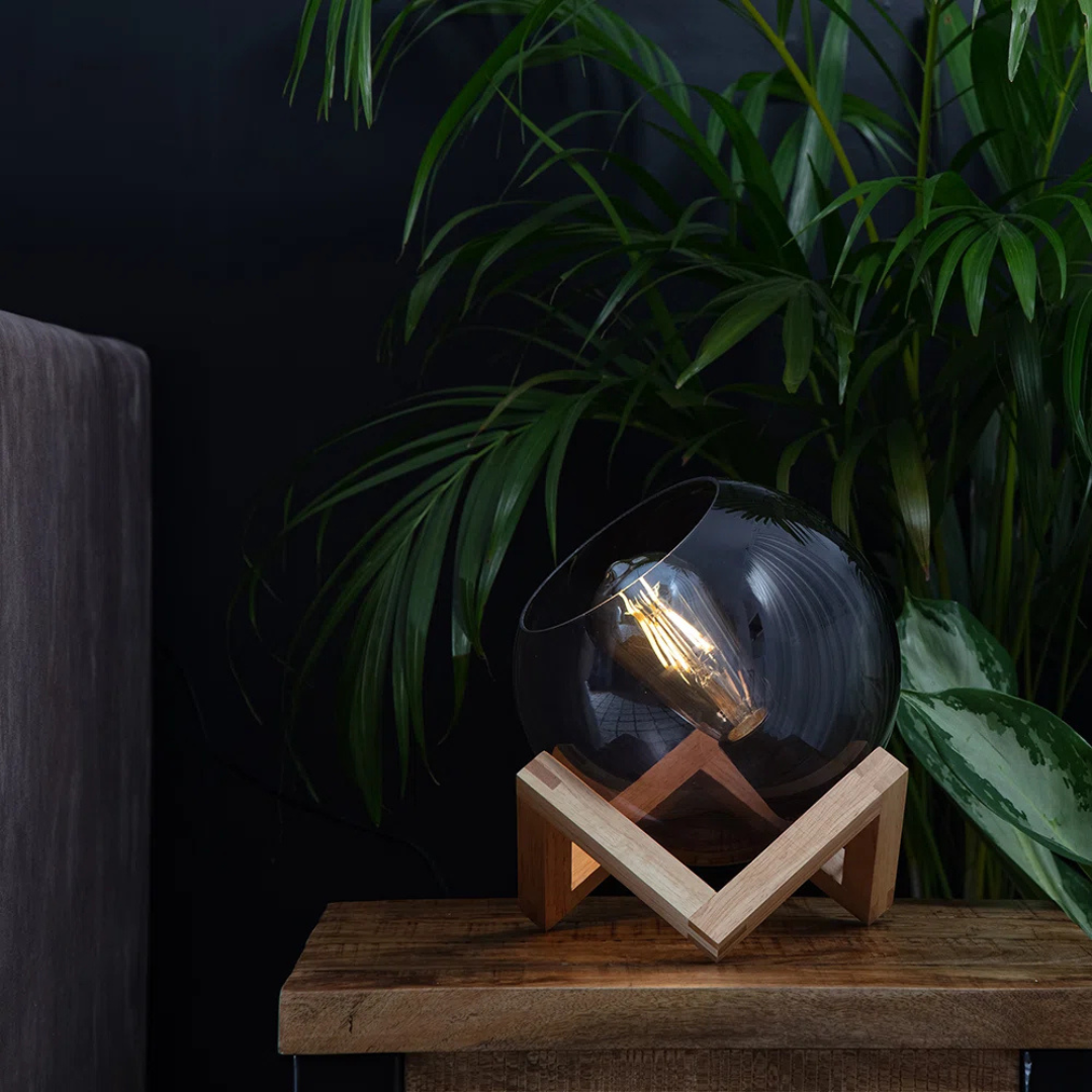 Decorative light bulb in a glass sphere on a wooden stand with plants in the background