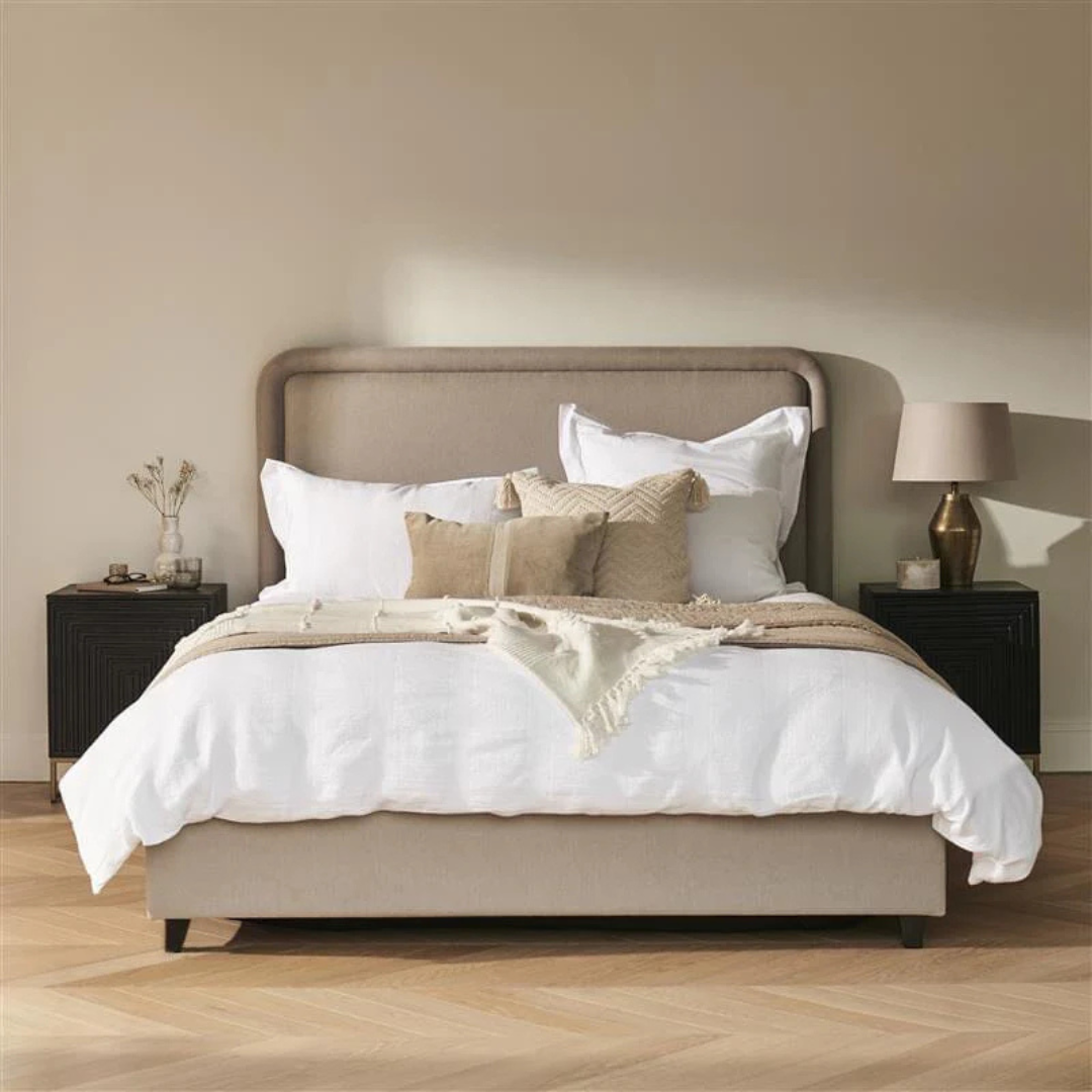 Neatly made bed with beige and white bedding in a bedroom setting.