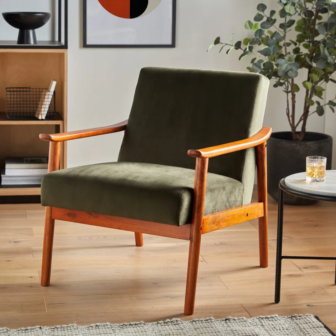 A olive green velvet armchair in a mid century living room. Front view