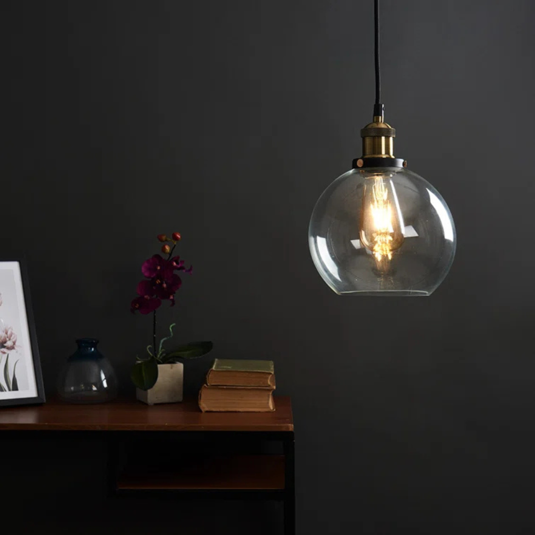 Clear glass pendant light hanging against a dark wall with a wooden shelf below.