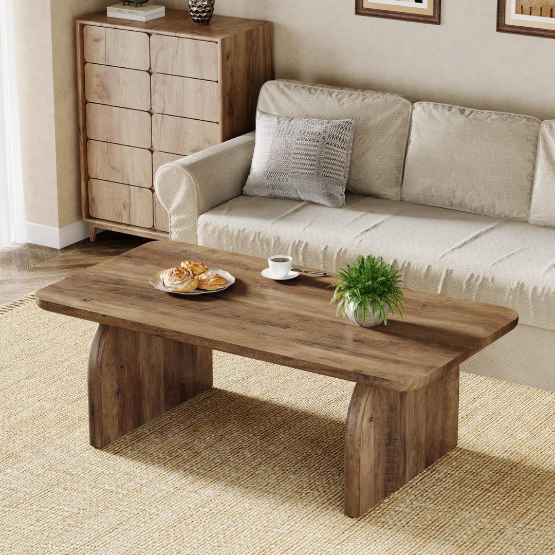 Wooden coffee table with a plate of pastries, a cup, and a plant in a living room setting.