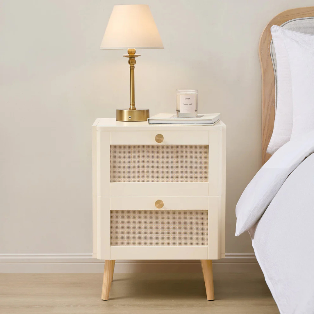 Beige nightstand with a lamp and candle next to a bed in a bedroom setting