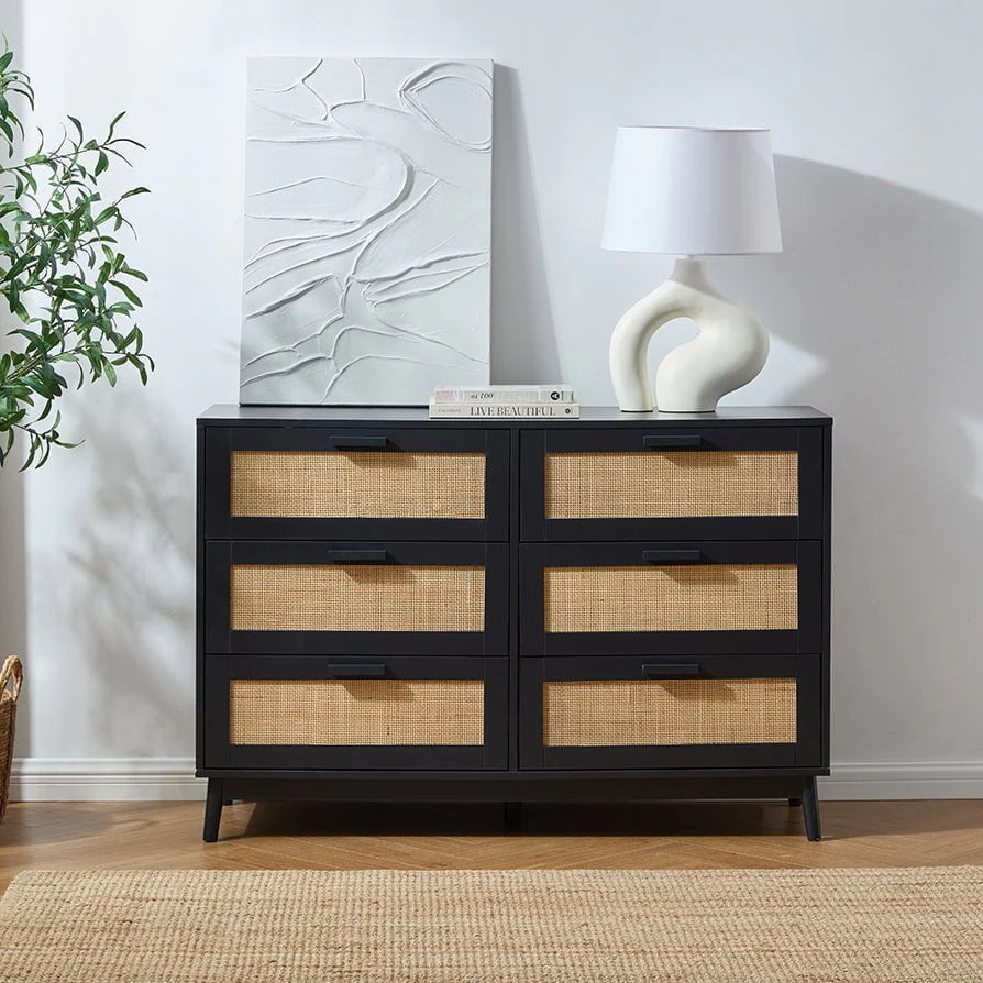 Black dresser with wicker drawers in a room with a lamp and abstract art on the wall.