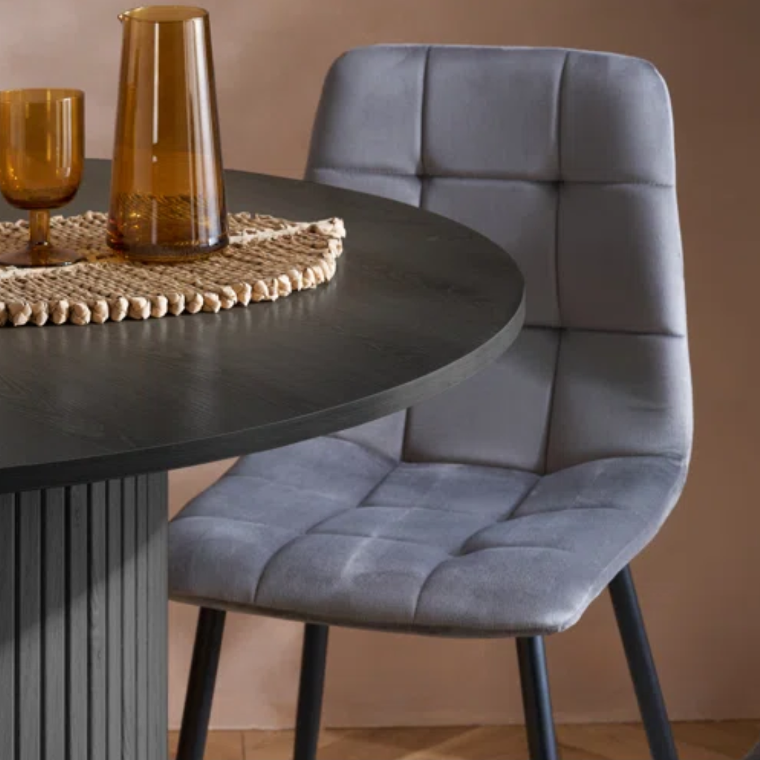 Gray upholstered chair next to a round dark table with decorative items.