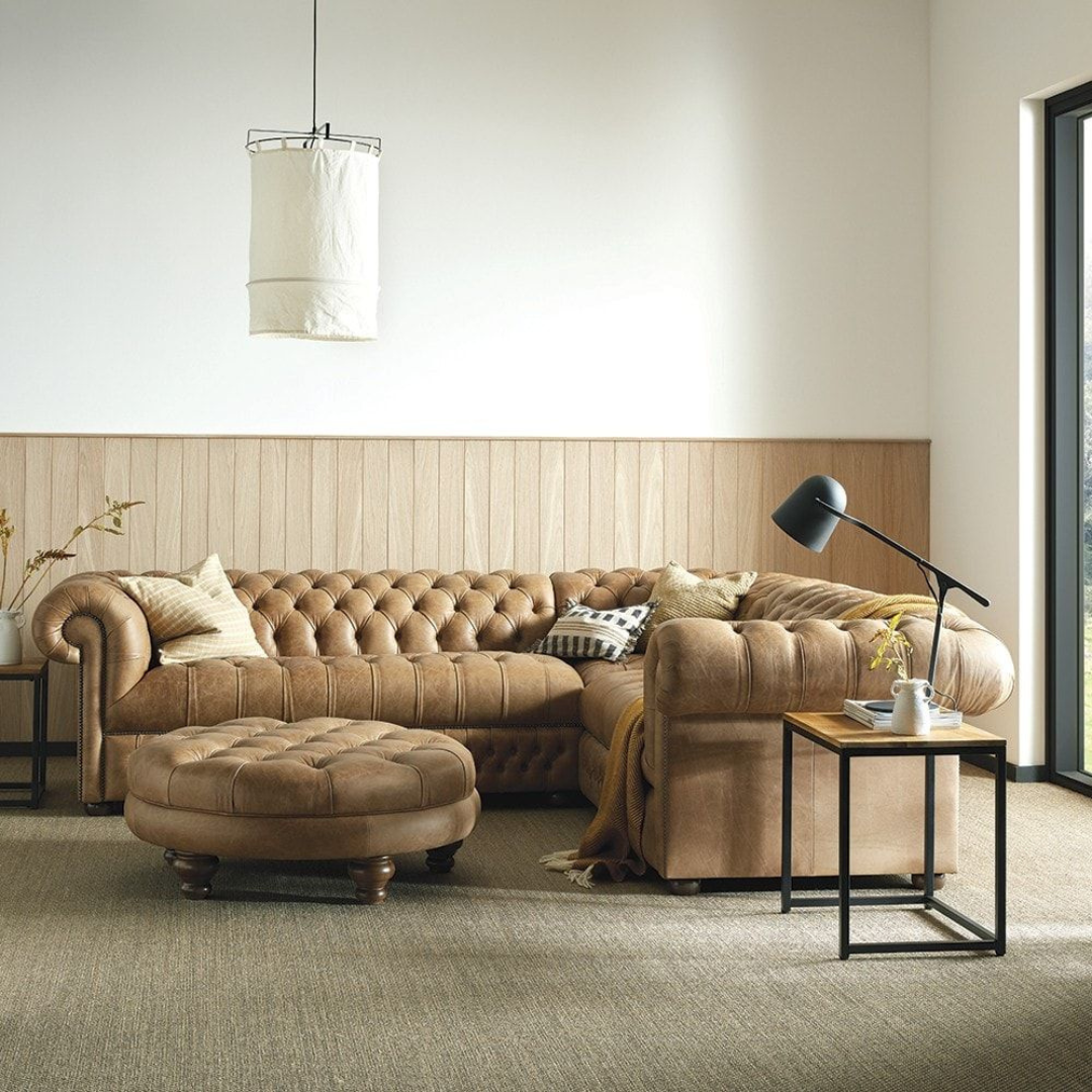 Image shows a beige chesterfield corner sofa. set in a modern home.