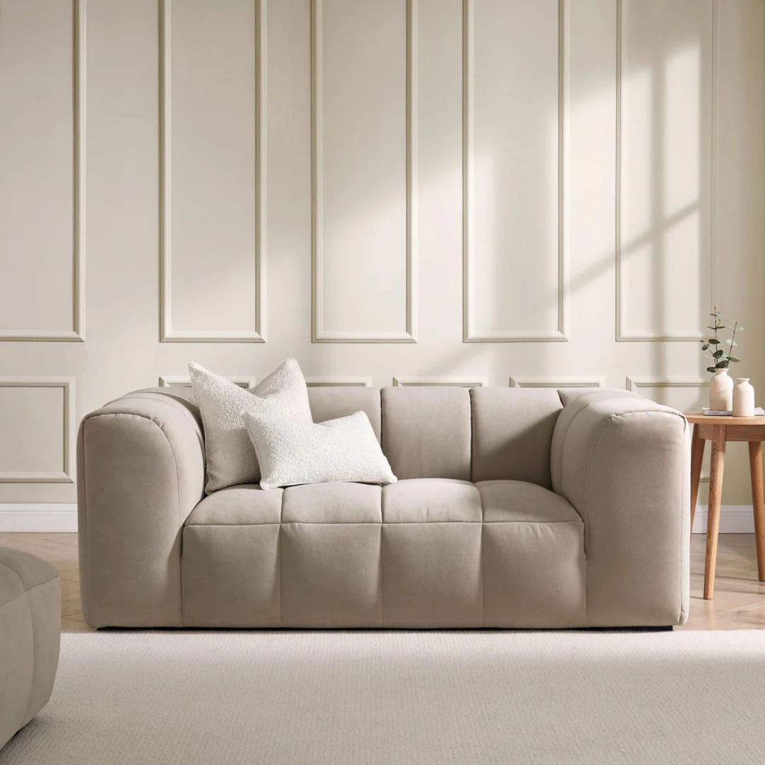 Image shows a contemporary beige 2 seater sofa set in a modern home with beige panelled walls.