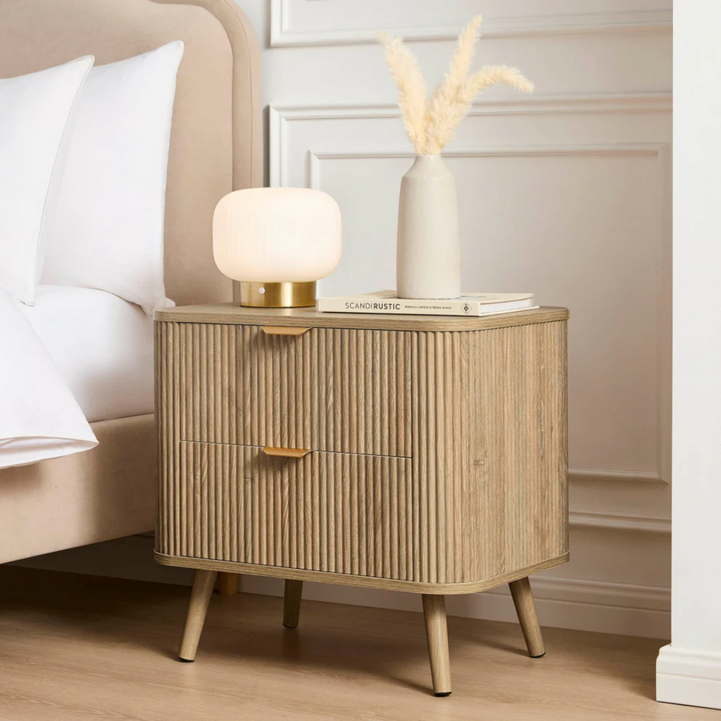 Wooden nightstand with lamp and vase in a bedroom setting