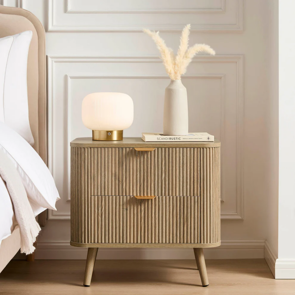 Beige nightstand with lamp and books against a white wall