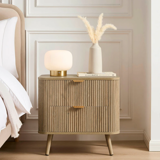 Beige nightstand with lamp and books against a white wall