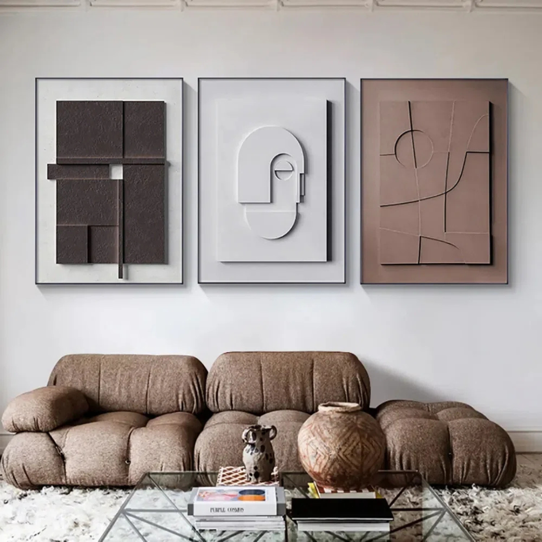 Three abstract artworks on a wall above a brown sofa in a living room.