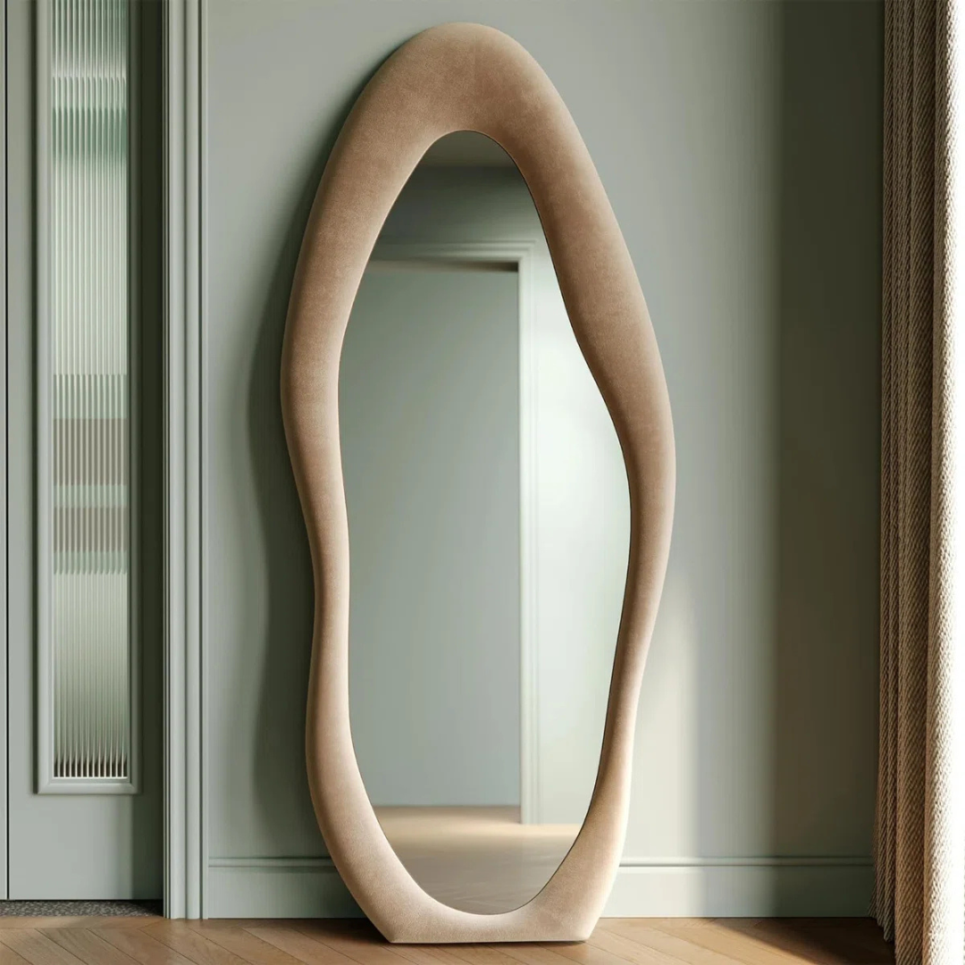 Modern oval mirror with a beige frame leaning against a light green wall.