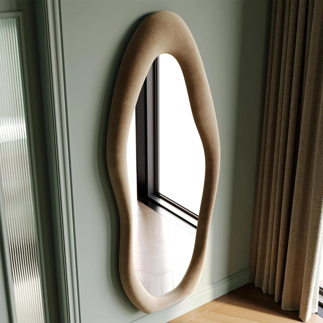 Modern wall mirror with a unique, curved beige frame in a room with a window and curtain.