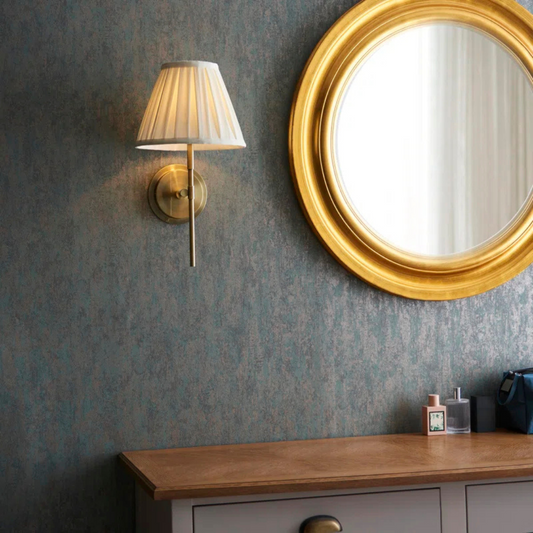 Gold-framed mirror and wall lamp on a textured wall with a wooden surface below.
