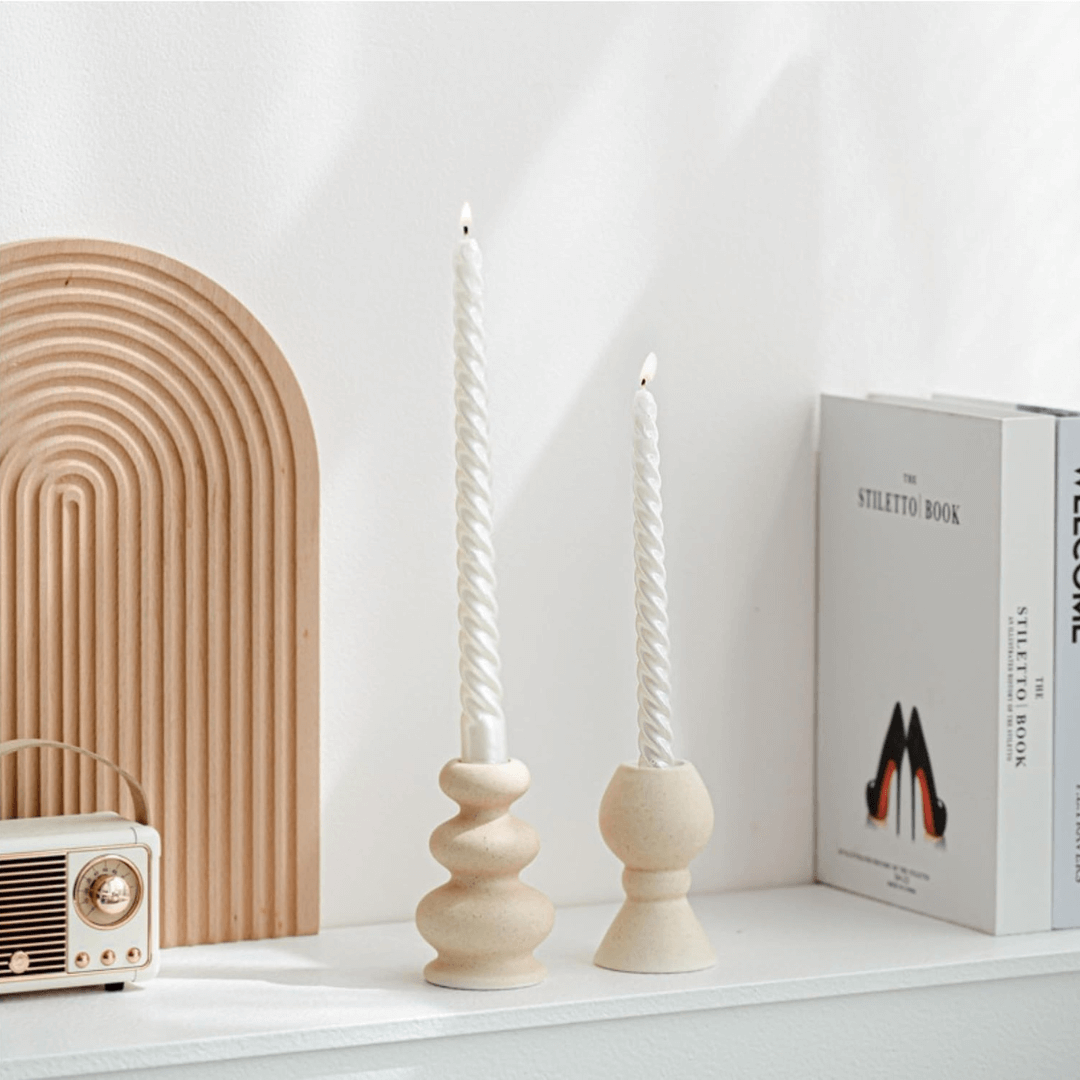 Two spiral candle holders on a shelf with a decorative arch and book in the background.