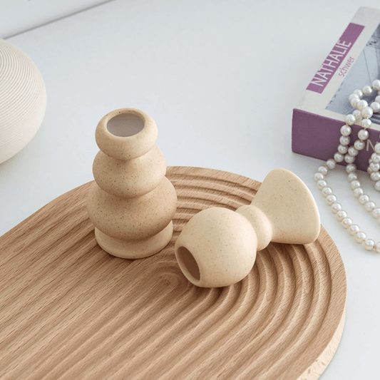 Two beige ceramic vases on a wooden surface with a magazine and pearls in the background.