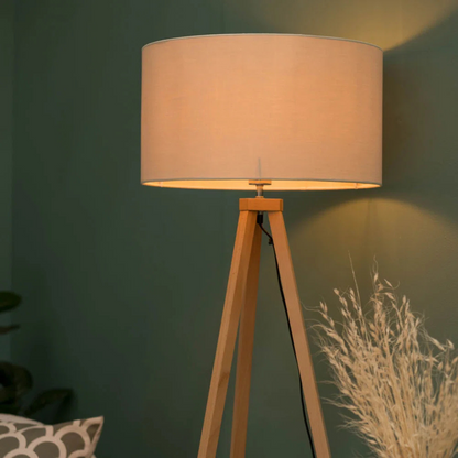 Floor lamp with beige shade and wooden tripod base against a green wall.