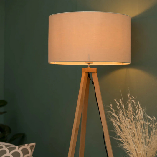 Floor lamp with beige shade and wooden tripod base against a green wall.