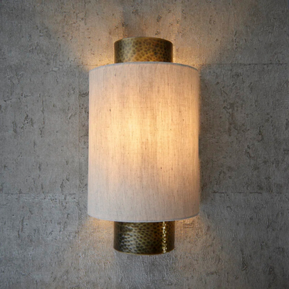 Wall-mounted light fixture with textured shade and metallic accents on a concrete wall.