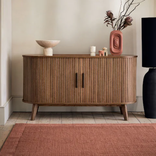 Wooden sideboard with decorative items in a room with a red rug and black lamp.