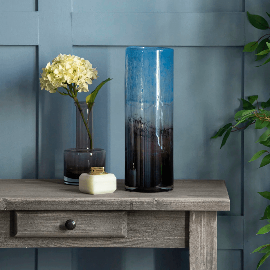 Tall cylindrical vase with gradient design on a wooden table against a blue wall.