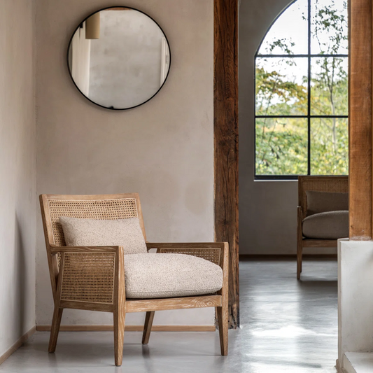 Wooden armchair with woven backrest in a room with a large window and round mirror.