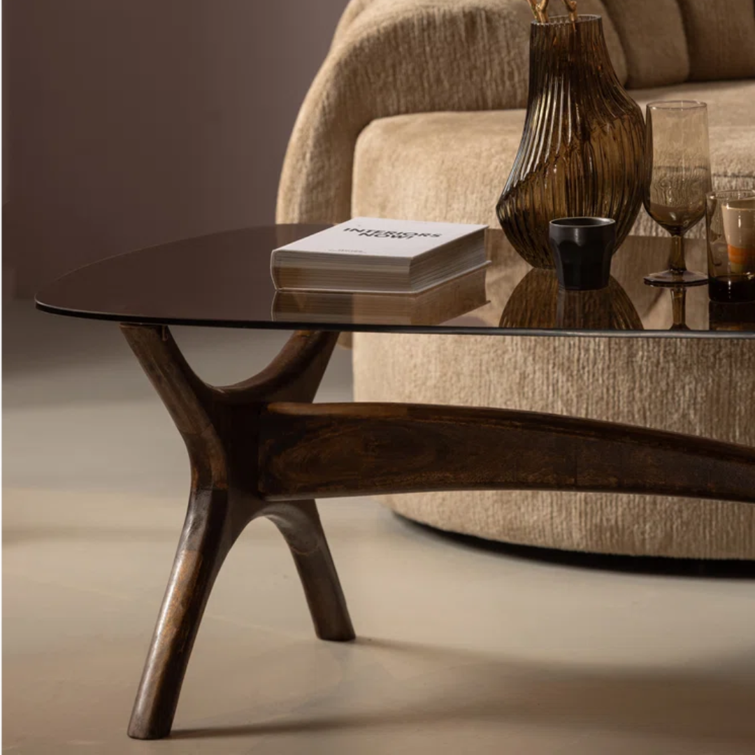 Modern coffee table with glass top and wooden legs in a living room setting.