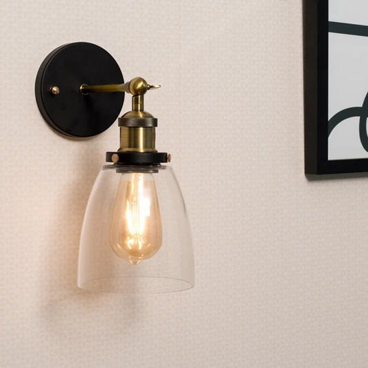 Wall-mounted light fixture with a clear glass shade and visible bulb on a neutral wall.