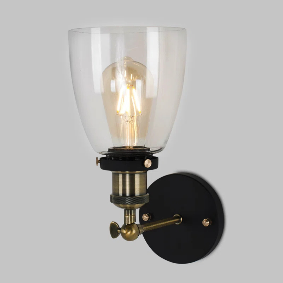 Wall-mounted light fixture with clear glass shade and brass accents on a gray background