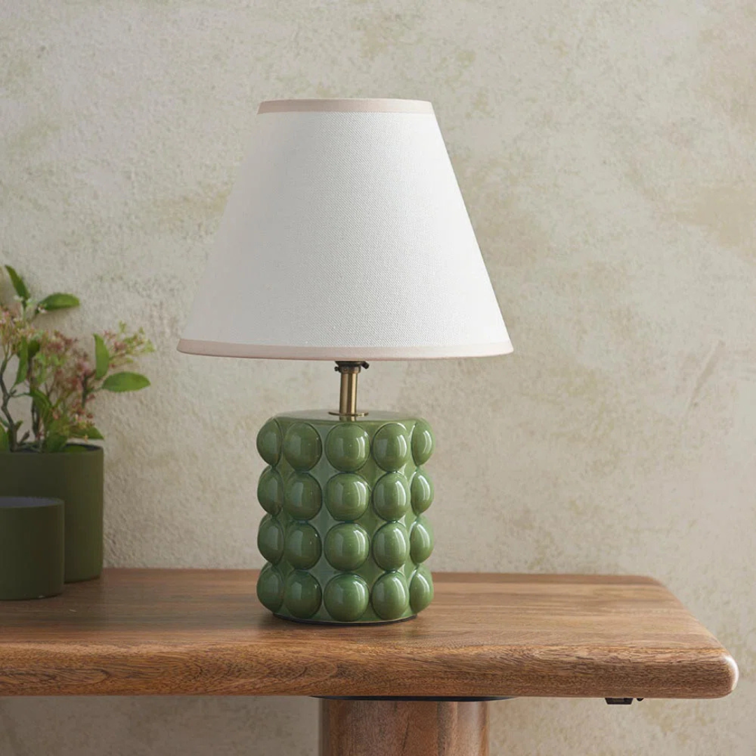 Green textured table lamp with white shade on a wooden surface.