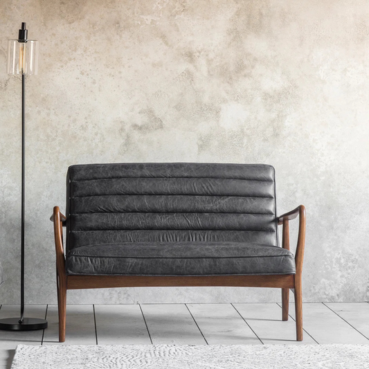 Gray cushioned sofa with wooden frame against a textured wall.