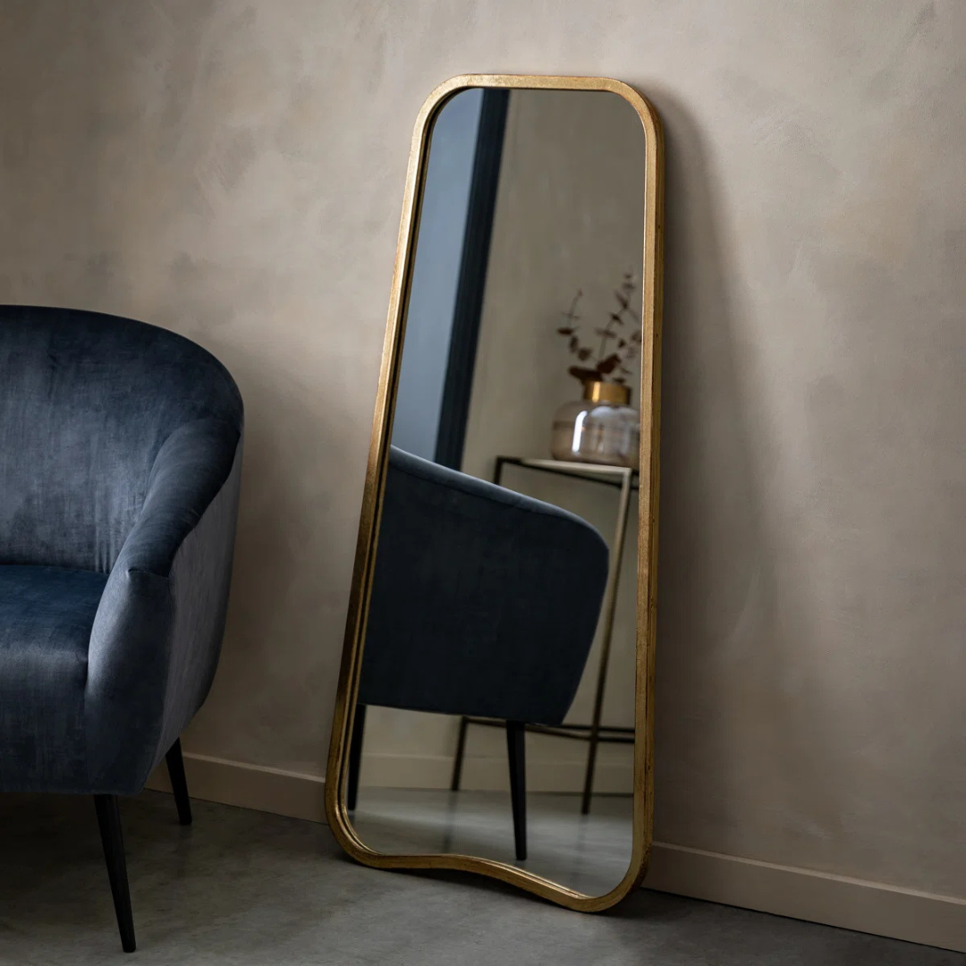 Gold-framed mirror leaning against a wall next to a blue armchair.