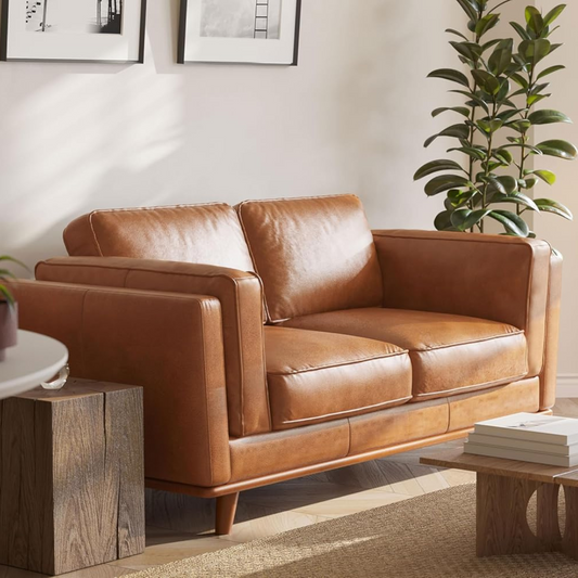 Brown leather sofa in a living room setting with a plant and wooden coffee table.