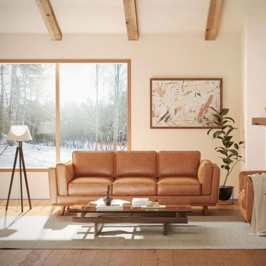 Brown leather sofa in a living room with a snowy landscape view through the window.