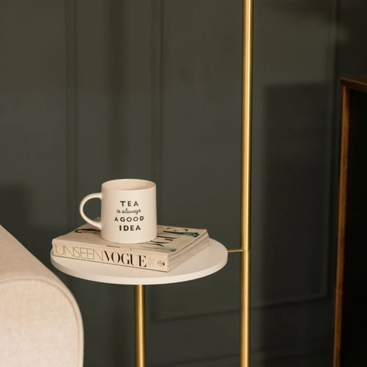 White mug with text on a book on a small round table next to a sofa.