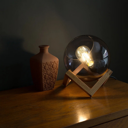 Glass orb with light bulb inside on a wooden stand next to a textured vase on a dark surface