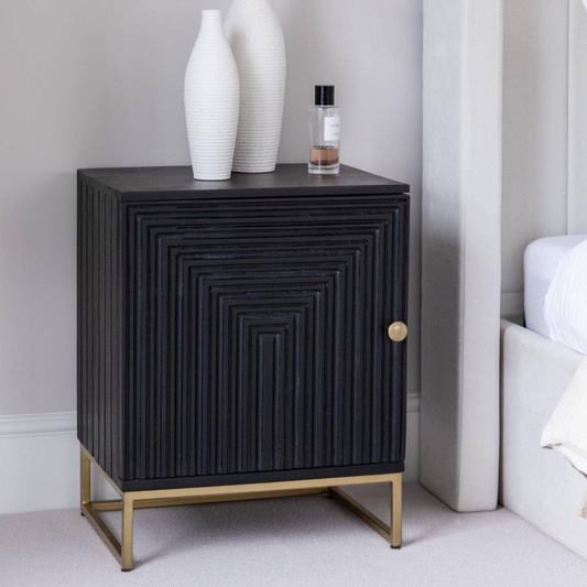 Black textured side table with gold legs in a bedroom setting