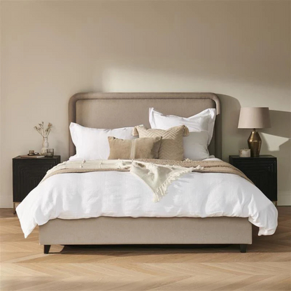 Neatly made bed with beige and white bedding in a bedroom setting.