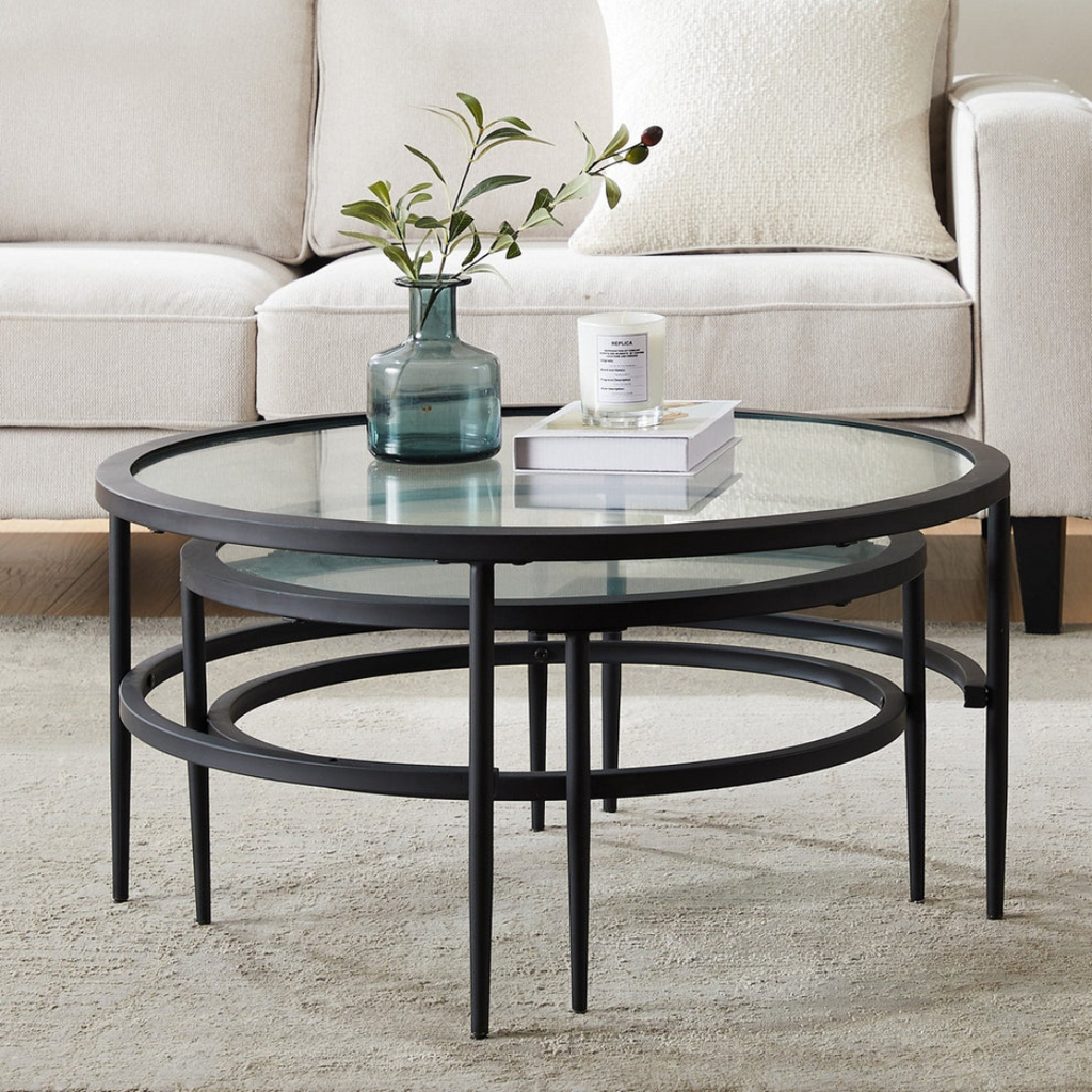 Round glass coffee table with black metal frame in a living room setting.