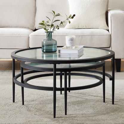 Round glass coffee table with black metal frame in a living room setting.