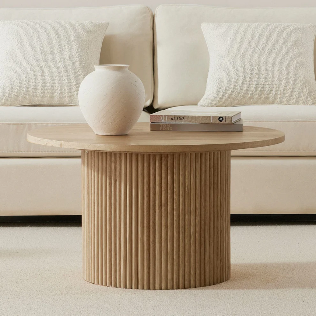 Wooden side table with a vase and books against a beige sofa.