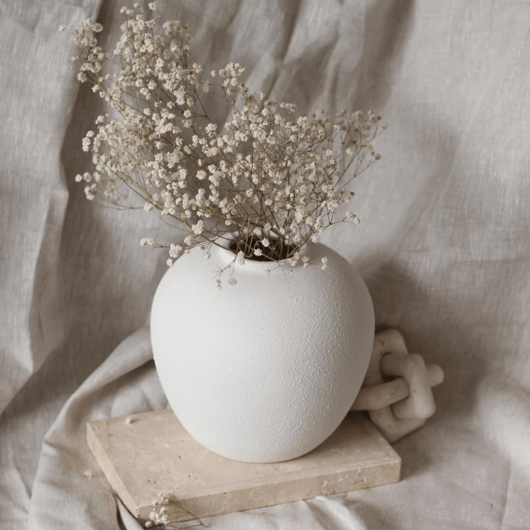 White textured vase with dried flowers on a wooden block against a soft beige fabric background